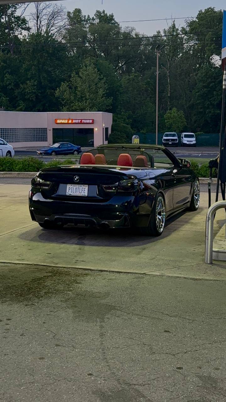 Rear three-quarter of the founder's BMW 440i with the top down — red interior visible
