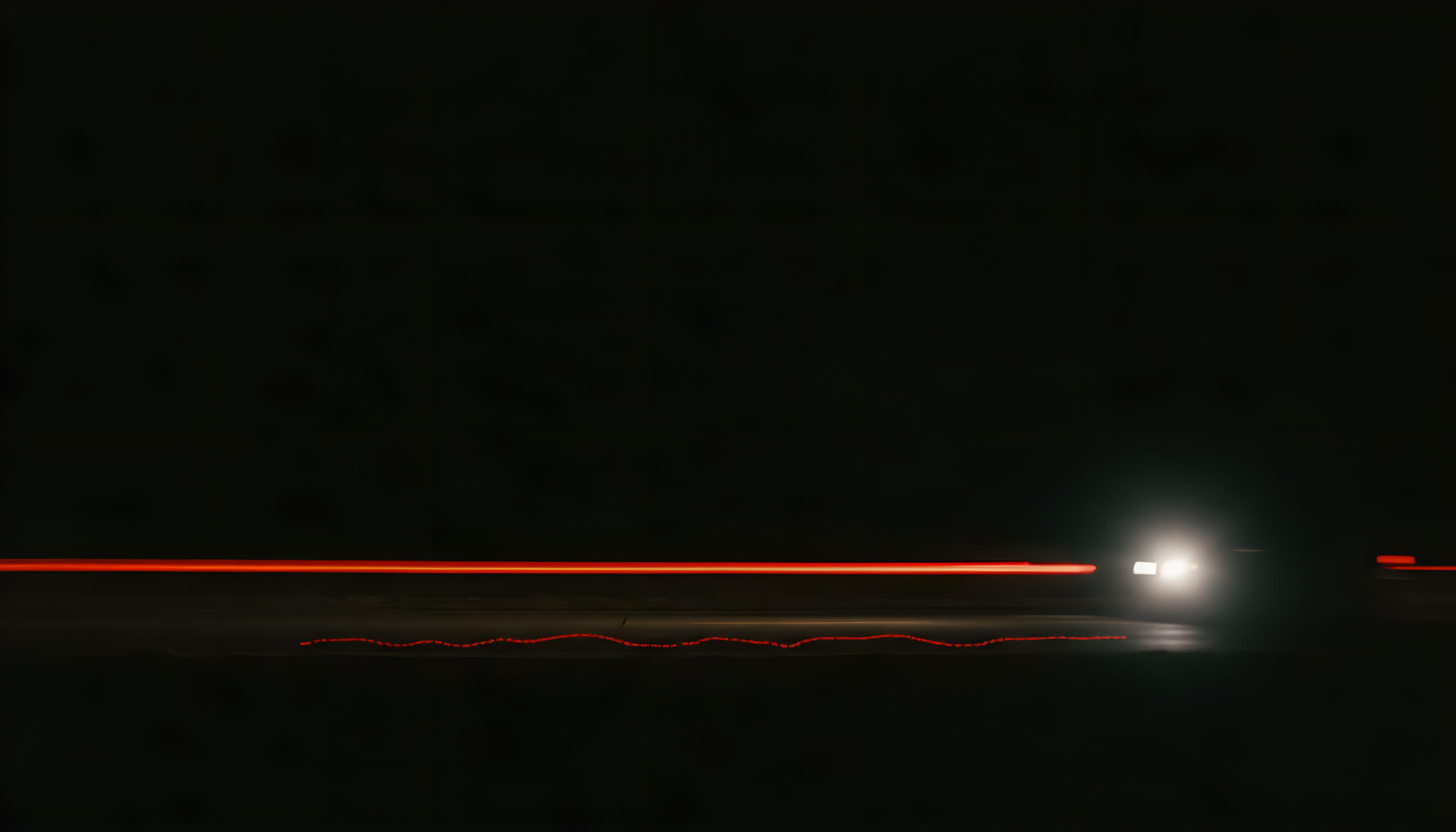 A lone car passing on a night road — headlight bloom and a single red taillight streak under a pure black sky